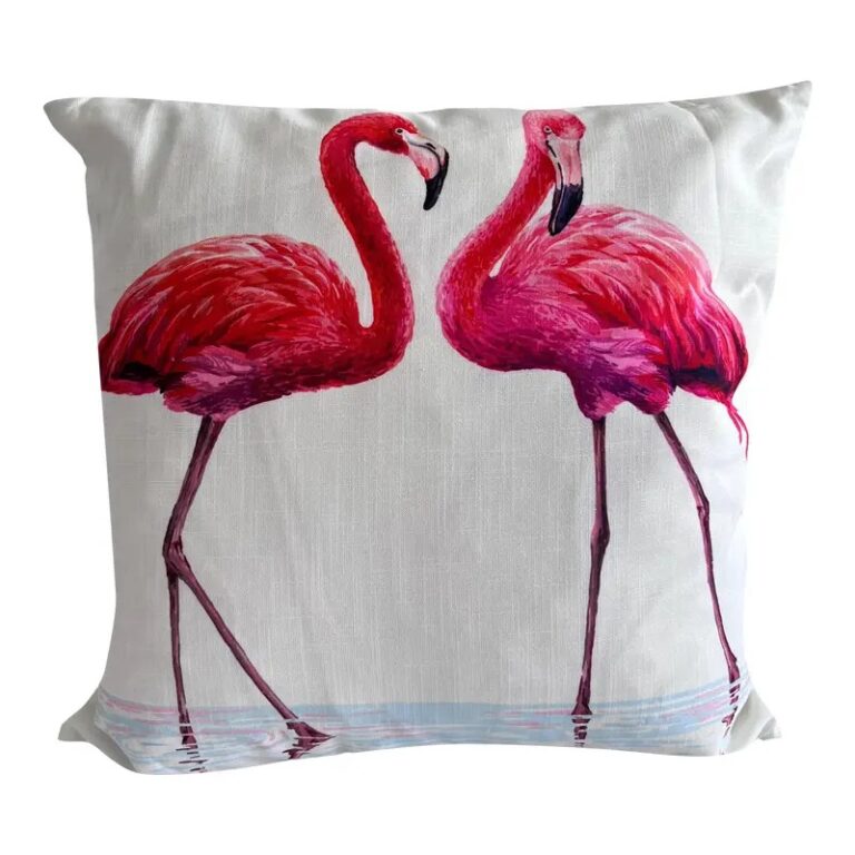A square white decorative pillow featuring a painterly illustration of two pink flamingos standing in light blue water.